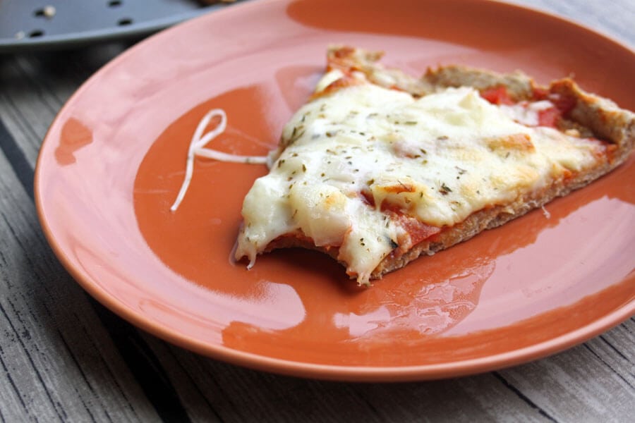 Whole Wheat Pizza slice on a plate with a bite removed.